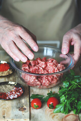The hands of the cook stir the raw minced meat in a bowl.