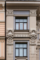 Vertical photo of detail of grey pink Art Nouveau building facade of two windows with dark frames and artsy decoration in Riga, Latvia, Europe
