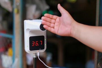 A fever meter with a stand and a man's hand is measuring fever in public areas