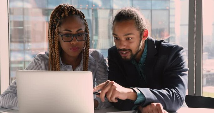 African ethnicity colleagues sit at workplace looking at laptop screen discussing collaborative project. Mixed-race female insurer speaking consulting making presentation to client. Mentoring concept