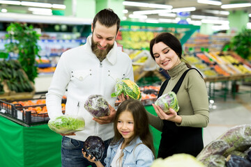 A young family with a daughter chooses vegetables in the supermarket.