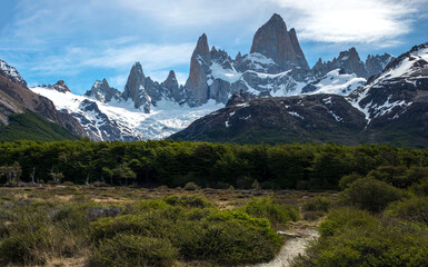 Panorama of Fitz Roy Rocky mountains with path heading to them trough the forest 