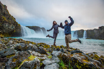 A couple at the bottom of the Godafoss waterfall with sunset in the background, Iceland