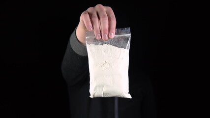 A man in a balaclava mask stands with a pack of heroin. A gangster holds out a drug bag toward the camera. On a black background.
