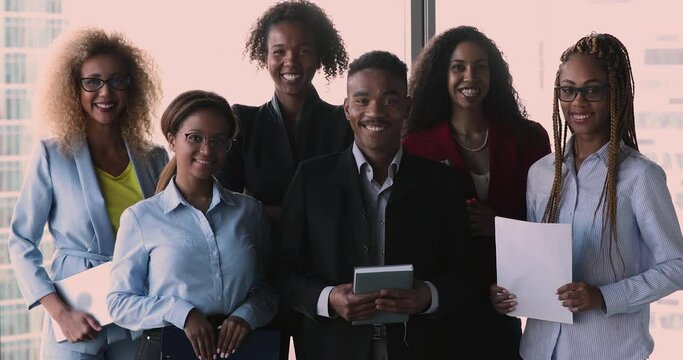 Six African ethnicity confident ambitious businesspeople smile look at camera pose in modern skyscraper office. Employees ready for business negotiations. Teamwork, successful company members portrait