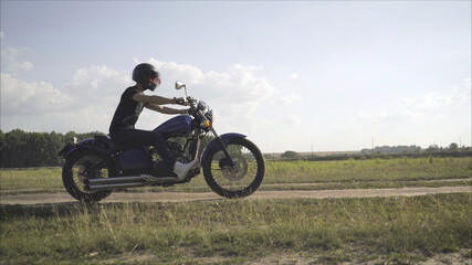 Plakat Motorcyclist rides on the field. The concept of adventure. Motorcyclist rides on a country road in the summer.