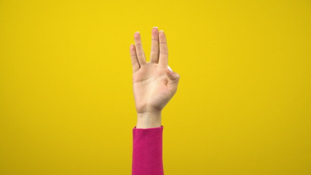 A female hand shows an alien greeting sign. Studio photography on an isolated yellow background.