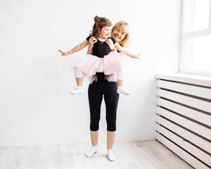 Woman mom indulges in dancing with her little daughter, is engaged in gymnastics in white interior, lifestyle photo at home