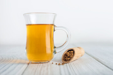 uncooked buckwheat in white plate and wooden scoop, on a white background close-up. Buckwheat tea and granules. Tea in transparent cup. Space for text.