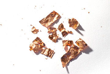 Shiny pieces of gold leaf on a white background. Gold sweat lies on a white table.