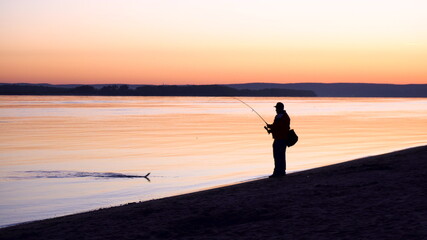 Fototapeta premium A man caught a fish. A silhouette of a man fishing at sunrise by the river. The yellow sun rises from the horizon.