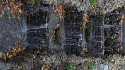 Water flows over an artificial waterfall in the park. Vertical video.