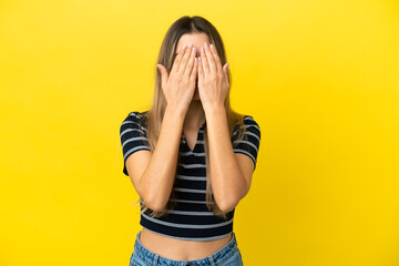 Young caucasian woman isolated on yellow background covering eyes by hands