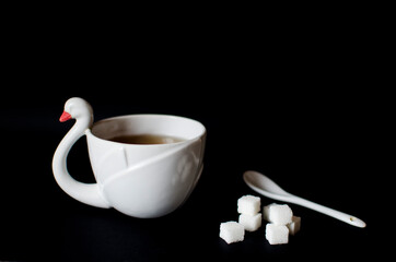 White cup of tea and cube sugar on black background