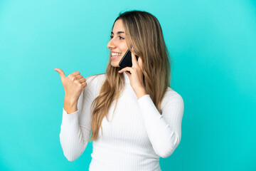 Fototapeta premium Young caucasian woman using mobile phone isolated on blue background pointing to the side to present a product