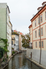 Fototapeta na wymiar Narrow canal, river between ancient houses in the old town in Prague, Czech Republic, Europe. European houses in greenery, with verandas and terraces.