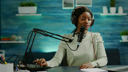 African influencer recording content using professional sound mixer and micophone in home studio. Speaking during livestreaming, blogger discussing in podcast wearing headphones.