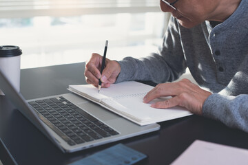 Student writing on notebook during studying online class. Asian casual business man working on laptop computer at home office