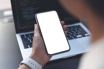 Mockup image of woman hand using blank screen mobile phone during working on laptop computer on office table