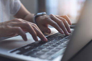 Close up of woman hands typing on laptop computer keyboard on table with sunlight