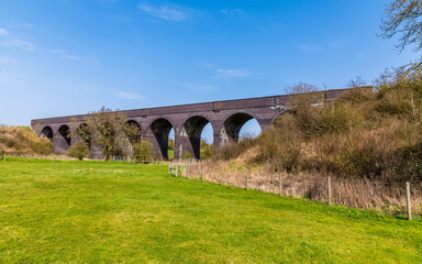 Fototapeta na wymiar A view from the corner of a field towards the abandoned Helmdon viaduct on a bright Spring day