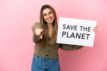 Young caucasian woman isolated on pink background holding a placard with text Save the Planet and pointing to the front