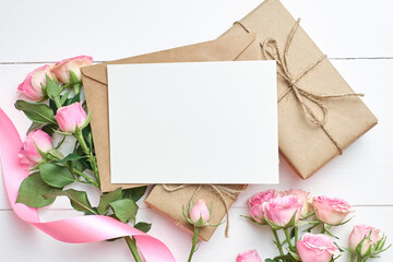Greeting card mockup with fresh roses and gift boxes on white wooden background