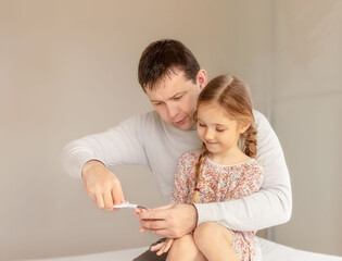 Dad cutting nails for his happy daughter. Father doing hygiene for his child.