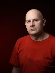 Studio portrait of middle-aged man serious face looking at camera isolated on dark red light background