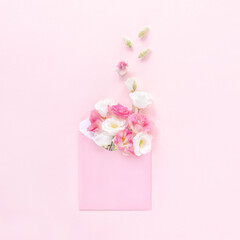 Open pink envelope full of spring flowers on pink background. Top view. Greeting card with eustoma flowers. Concept of spring.