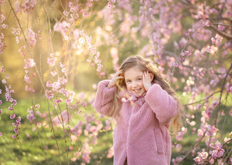 Little smiling girl in blooming sakura park. Happy 5 years old preschooler in blooming park in spring.