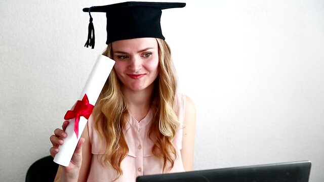 Woman student in masters after online exam, dancing with diploma behind a laptop. Online education, graduation