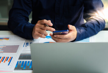 businessman hand using smartphone technology calculate for analysis and budget financial accounting with growth statistics chart and graph on paper work