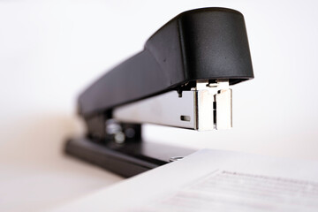 Close-up front view of a black stapler stapling several sheets of paper together. On white...