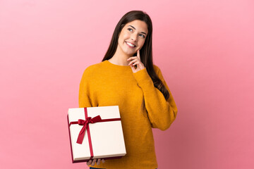 Teenager Brazilian girl holding a gift over isolated pink background thinking an idea while looking up