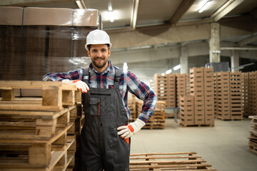 Portrait of warehouse worker standing by wooden palette in factory storage room.