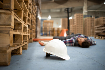 Injury at work. Warehouse worker lying unconscious on the concrete floor after the fall. Focus on...