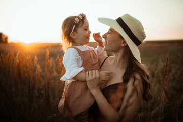 Stylish charming Caucasian young mother and daughter Toddler hugged in summer at sunset, family values and motherhood, brown toning