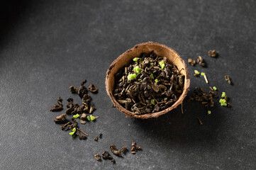 green dry tea leaf with sausep fruit in a coconut bowl with scattered leaves, gray background, close-up, top view