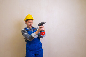 A girl in a blue construction worker's overalls and a yellow helmet holds a screwdriver in her hands and aims as if from a pistol
