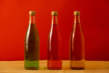 Three bottles of lemonade stand on a red background on a decorated wooden table. Yellow, green and red drink