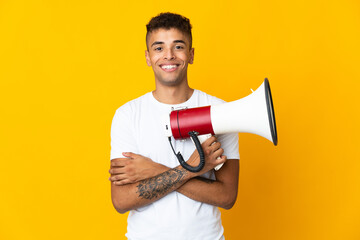 Young brazilian man isolated on yellow background holding a megaphone and smiling
