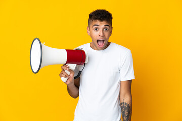 Young brazilian man isolated on yellow background holding a megaphone and with surprise expression