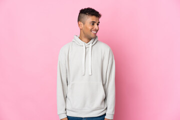 Young Brazilian man isolated on pink background looking to the side and smiling