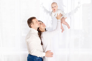 mom and dad lift a newborn baby up at home by the window, happy loving family concept, lifestyle