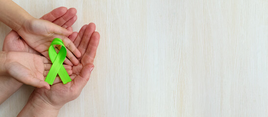 World Mental health awareness day.Adult and child hands holding Green Ribbon on white panoramic background.Organ donation.World kidney day. Banner. Copy space. Layout. Mock up