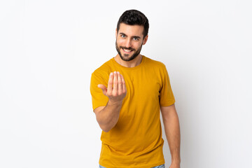 Young handsome man with beard isolated on white background inviting to come with hand. Happy that...