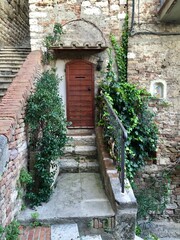 Fototapeta na wymiar Italian house. Fragment of facade of old house with wooden door. Stone wall, medieval building. Photo made in Umbria. Plant in pot. Ivy.