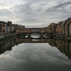 Fototapeta premium Ponte Vecchio view in Florence. Twilight the golden bridge view in Florence. Italy. River Arno, gray sky, reflection. Tuscany, Toscana