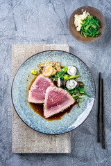Modern style traditional Japanese tuna tataki with vegetable and sushi maki rolls served as top view on a design plate with copy space PRO06828